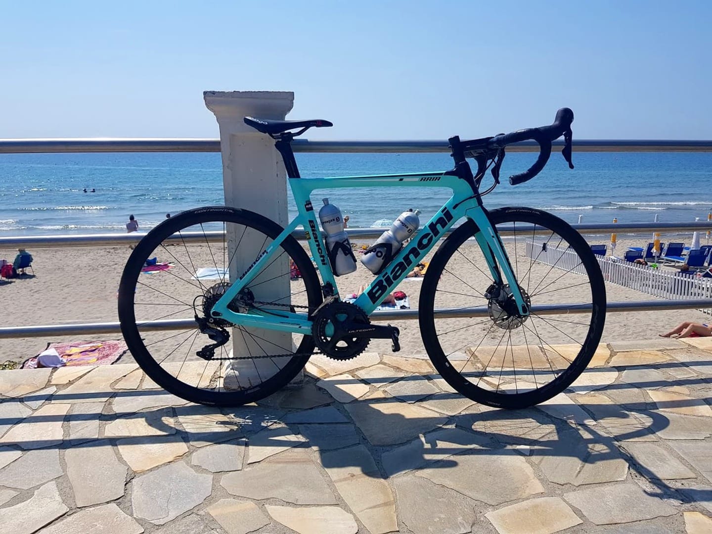 Rennradreise Italien Ligurien Blumenriviera, an einem Geländer am ligurischen Strand abgestelltes Biachi-Rennrad mit zwei Trinkflaschen