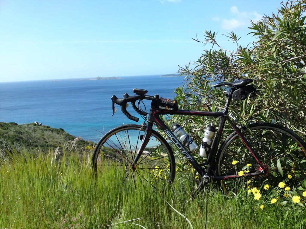 Rennradreise Italien Sardinien, an einem Busch abgestelltes schwarzes Scott-Rennrad mit Blick auf das Mittelmeer im Hintergrund