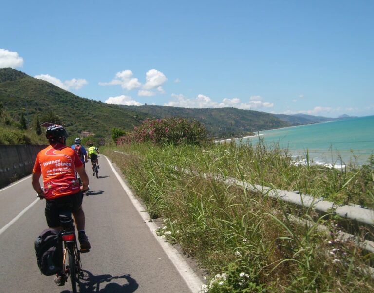 Radreise von Rom nach Sizilien, Mitglieder einer Launer-Radreisegruppe radeln auf einer Nebenstrasse entlang der Mittelmeerküste mit Blick auf das Meer und die Berge