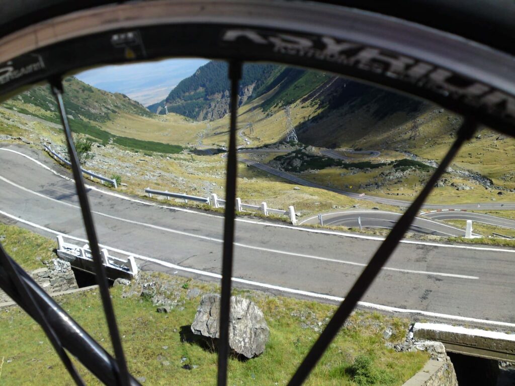 Rennradreise Rumänien Karpaten, Blick durch die Speichen eines Laufrades auf die sich zum Balea-Pass (2042m) hochschlängelnde Transfagarasche Hochstrasse