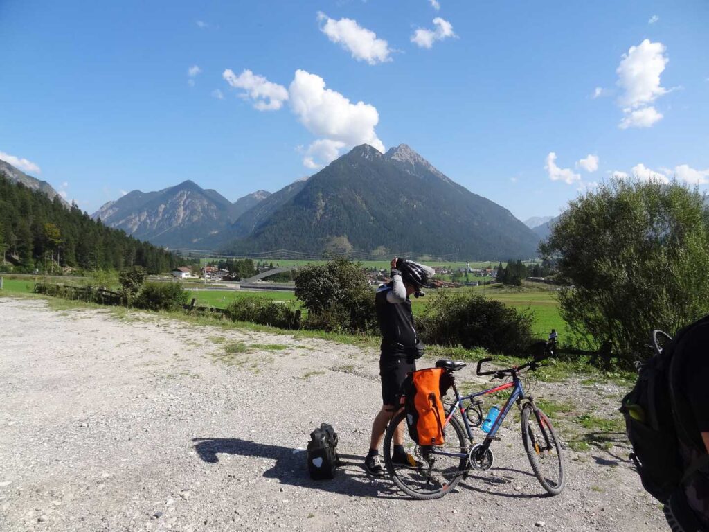 Radreise Deutschland Österreich Italien Via Claudia Augusta, Trekkingradler an seinem Rad stehend vor einem Alpental mit den Bergen im Hintergrund